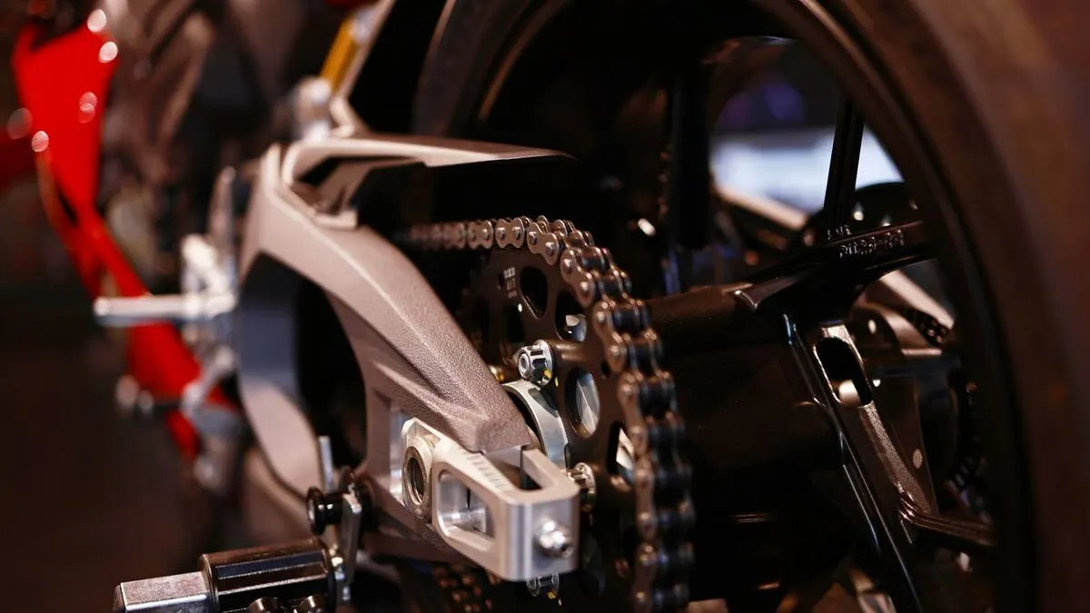 Mains gantées tenant une chaîne de moto neuve près du pignon, atelier lumineux et outillage