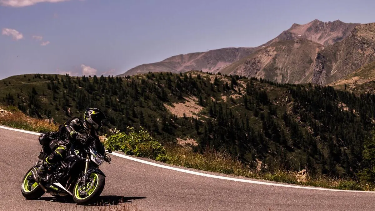 Motard traversant un col de montagne sous le soleil, route sinueuse, paysage sec et ombres marquées